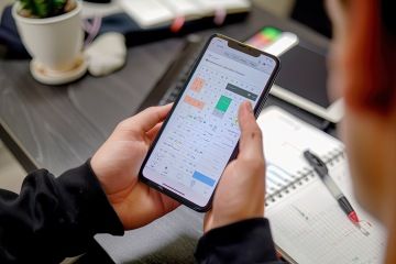 Student pracuje s tabulkou na mobilním telefonu, vedle má sešit s poznámkami.